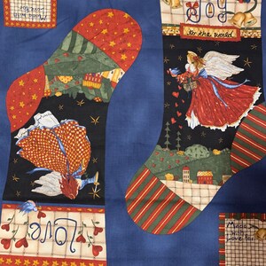 May include: Christmas stocking fabric with a blue background. The fabric features two stocking shapes with angel and village scenes. One stocking has the word "Joy" and "to the world" printed on it. The other stocking has the word "Love" printed on it.