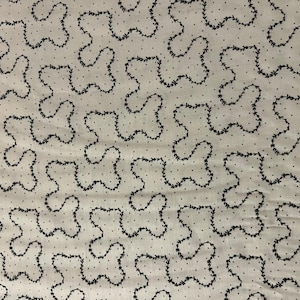 May include: Cream-colored fabric with a repeating pattern of black, stylized floral shapes and small black dots. The design creates a textured, organic feel, suitable for various textile applications.