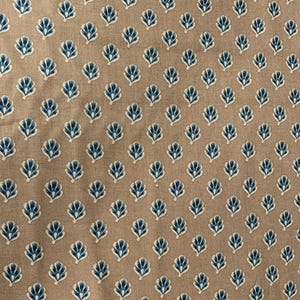 May include: Close-up of a tan fabric with a repeating pattern of blue and white stylized floral designs. The pattern is evenly spaced across the fabric, creating a visually appealing texture. The fabric appears to be cotton or linen.