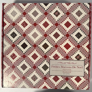 May include: A square box with a repeating pattern of red, cream, and brown geometric shapes. The pattern includes squares and diamond shapes. The box has a label that reads "moda Petites Maisons De Noel".