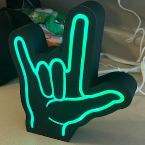 May include: A black light-up sign in the shape of a hand making the 'I love you' sign. The sign is lit up in a bright green color.