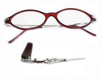 May include: Oval-shaped eyeglasses with a deep red frame and silver-toned temples. The lenses are clear, and the arms are thin and extend to the ear pieces. The temple detail is ornate.