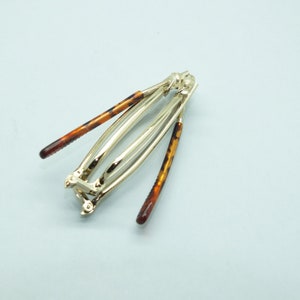 May include: A silver hair clip with two tortoise shell barrettes attached. The clip is open and ready to be used.