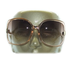 May include: A pair of large, brown, plastic framed sunglasses with brown tinted lenses. The sunglasses are on a mannequin head.