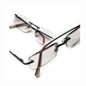 Puede incluir: Un par de gafas negras sin montura con lentes transparentes. Las gafas están dobladas por la mitad, con un lado del marco apoyado sobre el otro.