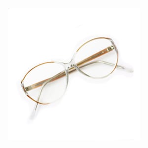 Puede incluir: Gafas de plástico transparente con patillas de metal marrón. Las gafas tienen una forma redondeada y ovalada.