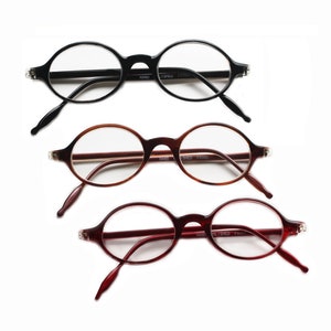 May include: Three pairs of round reading glasses with black, brown, and burgundy frames. The glasses are all in focus and the frames are clearly visible. The glasses are all in a neutral position, not being worn.