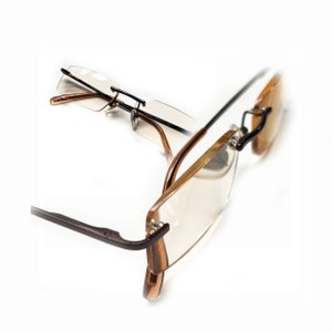 May include: A pair of rimless glasses with a brown frame and clear lenses. The glasses are made of metal and plastic.