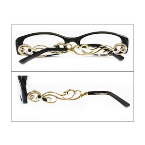 May include: Black eyeglasses with gold-tone ornate metal accents on the arms. The glasses have a rectangular shape and a black frame.