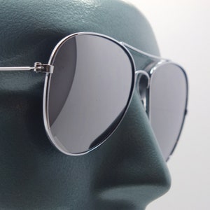 Könnte beinhalten: Silberne Aviator-Sonnenbrille mit dunkelgrauen Gläsern. Die Sonnenbrille sitzt auf einem Mannequin-Kopf.