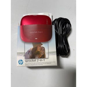 May include: A red HP Sprocket 2-in-1 instant camera and photo printer. The device is on top of a box with the product name and a photo of two women. A black cable is next to the device.
