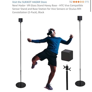 Puede incluir: Dos soportes altos de metal negro con bases circulares, diseñados para sensores de realidad virtual. Cada soporte cuenta con un poste vertical delgado y un soporte de montaje superior. Se incluye una estación base cúbica negra y un detalle de fijación.