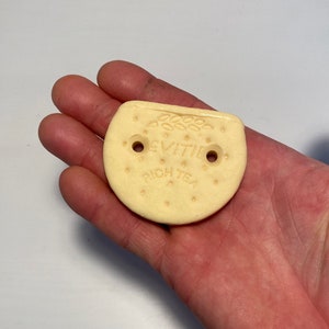 May include: A white, round, biscuit-shaped object with the words "Rich Tea" and "Evita" printed on it. There are two small holes on the object.