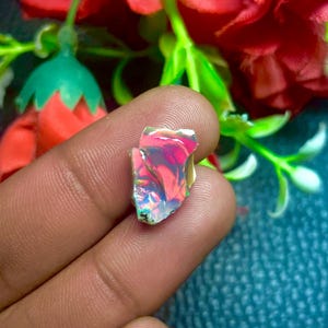 Könnte beinhalten: Ein kleiner, irisierender, rosa-blauer Opal-Edelstein mit einer rauen, unregelmäßigen Form.