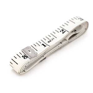 May include: A white tape measure with black markings, rolled up and showing the numbers 8, 1, INCH, and 2.