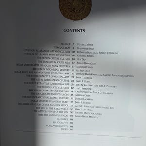 May include: A book's contents page with a list of topics related to the sun in various cultures. The page includes titles such as "The Sun in Japanese Art and Culture" and "The Aztecs: People of the Sun." A decorative sun emblem is at the top.