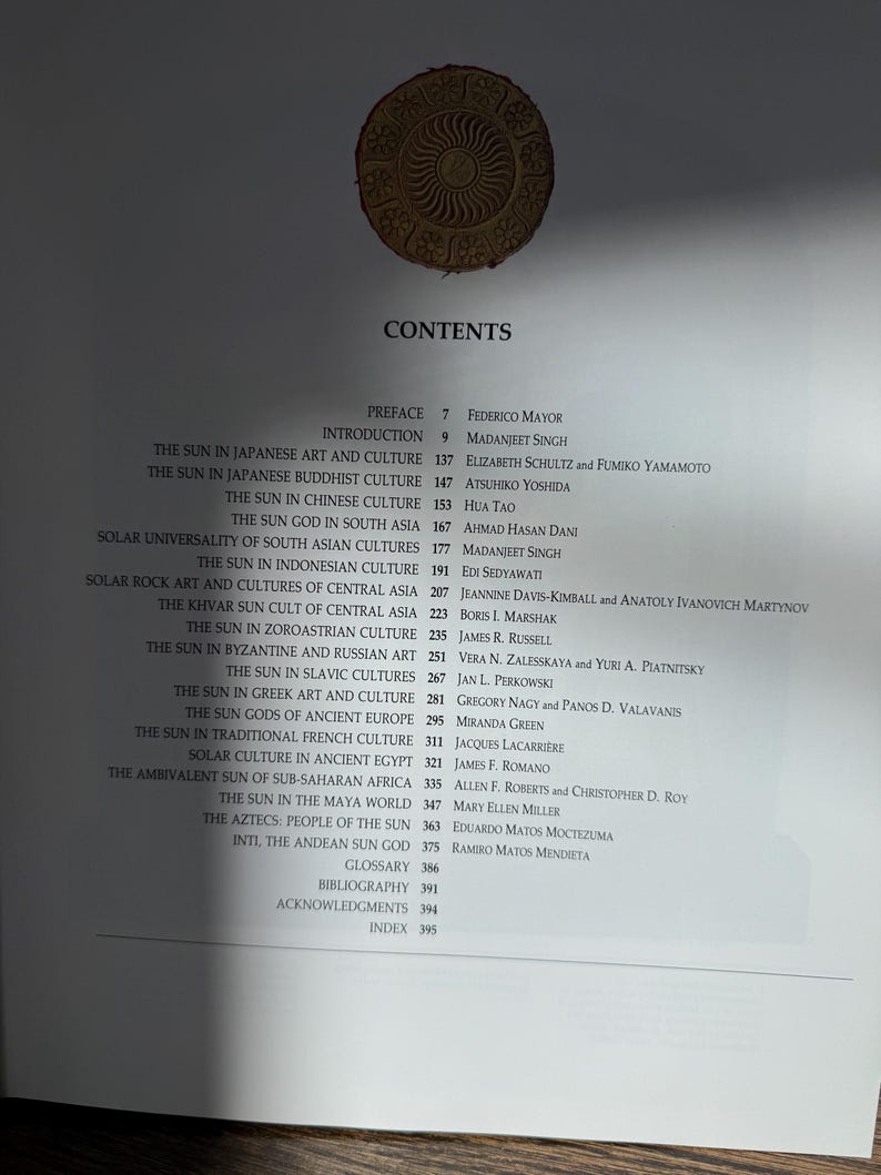 May include: A book's contents page with a list of topics related to the sun in various cultures. The page includes titles such as "The Sun in Japanese Art and Culture" and "The Aztecs: People of the Sun." A decorative sun emblem is at the top.