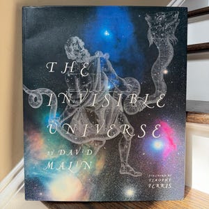 May include: A hardcover book titled "The Invisible Universe" by David Malin. The cover features a celestial illustration with a figure and constellations against a dark, starry background. The book has a foreword by Timothy Ferris.
