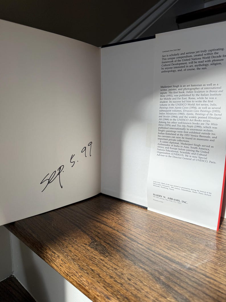 May include: An open book with text and a handwritten date, "Sep. 5.99," on the left page. The right page features text about the sun and Madanjeet Singh. The book is on a wooden surface.