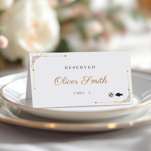 May include: A white place card with gold accents and text. The card reads "RESERVED" at the top, with "Oliver Smith" in elegant script below. "TABLE 2" is printed at the bottom, along with a small fish icon.