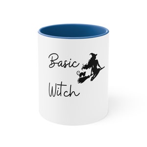 May include: White ceramic mug with a blue rim. The mug has a black silhouette of a witch flying on a broomstick with a black cat. The text "Basic Witch" is written in black cursive.