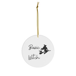 May include: White ceramic ornament with a black silhouette of a witch riding a broomstick with a black cat. The text "Basic Witch" is written in black cursive.