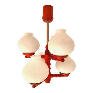 Può includere: Un lampadario vintage con una struttura in legno rosso e quattro paralumi in vetro bianco a forma di bulbo. L'apparecchio ha un'asta centrale e un design decorativo a forma di bambù. Il lampadario è progettato per essere montato a soffitto.