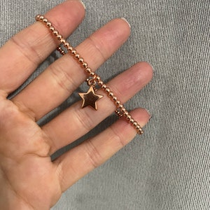 May include: A rose gold beaded bracelet with a star charm.