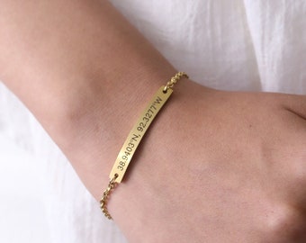 May include: Gold chain bracelet with a bar charm engraved with the coordinates "38.6403°N 92.3277°W".