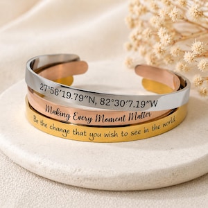 Peut inclure: Trois bracelets ouverts en argent, or rose et or. Le bracelet argenté porte les coordonnées 27°58'19.79"N, 82°30'7.19"W gravées. Le bracelet en or rose dit "Making Every Moment Matter". Le bracelet doré dit "Be the change that you wish to see in the world".