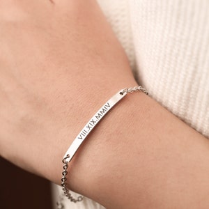 May include: A silver bracelet with a bar charm engraved with the Roman numerals "VIII.XIX.MMIV".