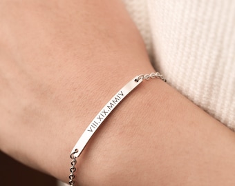 May include: A silver bracelet with a bar charm engraved with the Roman numerals "VIII.XIX.MMIV".