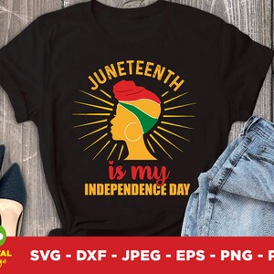 Op de afbeelding: Zwart t-shirt met de tekst "Juneteenth is my Independence Day" in geel en rood. Het ontwerp toont een profiel van een vrouw met een hoofddoek in rood, groen en geel, omringd door zonnestralen.