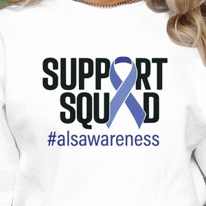 May include: White long-sleeve sweatshirt with a black graphic that says "SUPPORT SQUAD" with a blue ribbon in the middle and the text "#alsawareness" below.