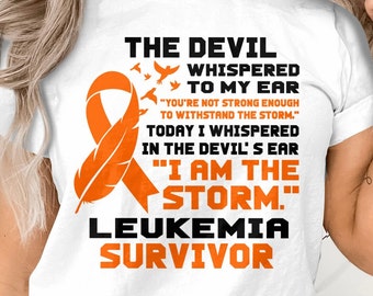 May include: White t-shirt with an orange ribbon and the text "THE DEVIL WHISPERED TO MY EAR "YOU'RE NOT STRONG ENOUGH TO WITHSTAND THE STORM." TODAY I WHISPERED IN THE DEVIL'S EAR "I AM THE STORM." LEUKEMIA SURVIVOR"