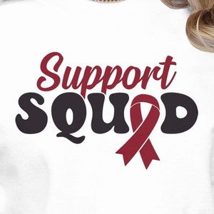 May include: White sweatshirt with the text "Support Squad" in black and red. A red ribbon is included in the text.