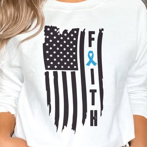 Peut inclure: Sweat-shirt blanc avec un motif de drapeau américain usé et le mot "FAITH" avec un ruban bleu au centre du "I".