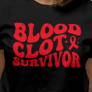 Op de afbeelding: Zwart T-shirt met rode tekst die "BLOOD CLOT & SURVIVOR" luidt in een retro lettertype. Het ampersand is versierd met een rood lint.