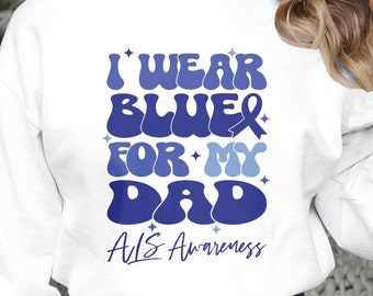 Op de afbeelding: Wit sweatshirt met een blauwe en lichtblauwe afbeelding met de tekst "Ik draag blauw voor mijn vader" met een blauw lint en sterren. De tekst "ALS-bewustzijn" staat onder de afbeelding.