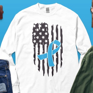 May include: White long-sleeve t-shirt with a distressed American flag design and a blue ribbon in the center.