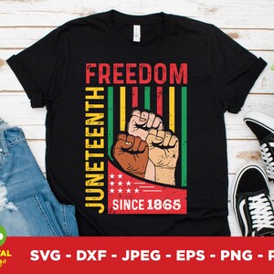Può includere: T-shirt nero con le parole "FREEDOM JUNETEENTH SINCE 1865" in rosso, giallo e verde. Il design include una grafica di pugni con diverse tonalità di pelle. La maglietta è mostrata con jeans blu e scarpe da ginnastica bianche e nere.
