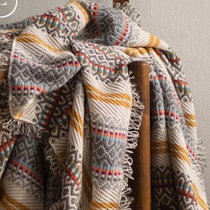 May include: A wooden chair with a woven blanket draped over it. The blanket has a geometric pattern in shades of gray, yellow, red, and blue.