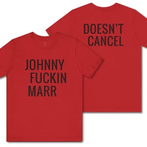 Peut inclure: Deux t-shirts rouges avec du texte noir. L'un dit "JOHNNY FUCKIN MARR" et l'autre "DOESN'T CANCEL". Les t-shirts sont présentés sur un fond blanc.