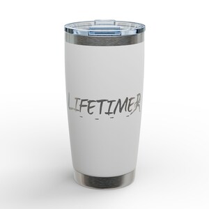 Op de afbeelding: Een witte roestvrijstalen beker met een zilveren rand en deksel. Het woord "LIFETIMER" is in een grijze, handgeschreven lettertype op de voorkant gedrukt. De beker is ontworpen om dranken warm of koud te houden.