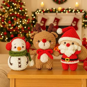 May include: Three handmade crochet Christmas figures: a snowman with red earmuffs and a green scarf, a reindeer with a red bow, and Santa Claus in a red suit and hat. The figures are on a wooden table with a Christmas tree in the background.