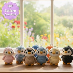 May include: A collection of handmade crochet penguin ornaments in various colors, including pink, blue, brown, and black. Each penguin has a yellow beak and a white belly. The image includes a "PDF Pattern Download" graphic.
