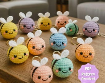 May include: A collection of colorful, crocheted bee keychains. Each bee has a smiling face, white wings, and a gold-colored keyring. The bees are in various colors, including yellow, orange, pink, blue, green, and purple. The image also includes a graphic that says "PDF Pattern Download."