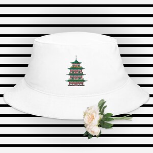 Pode incluir: Chapéu de pescador branco com uma pagoda verde e vermelha bordada na frente.