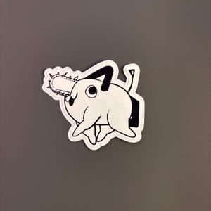 May include: A black and white sticker of a cartoon creature with a chainsaw for a mouth. The creature has a round body and a long tail.