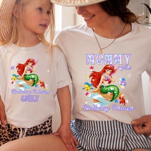 Peut inclure: T-shirts blancs avec un motif de sir&egrave;ne aux cheveux roux et &agrave; la queue verte. Les chemises affichent le texte "Birthday Princess" et "Mommy of the Birthday Princess".